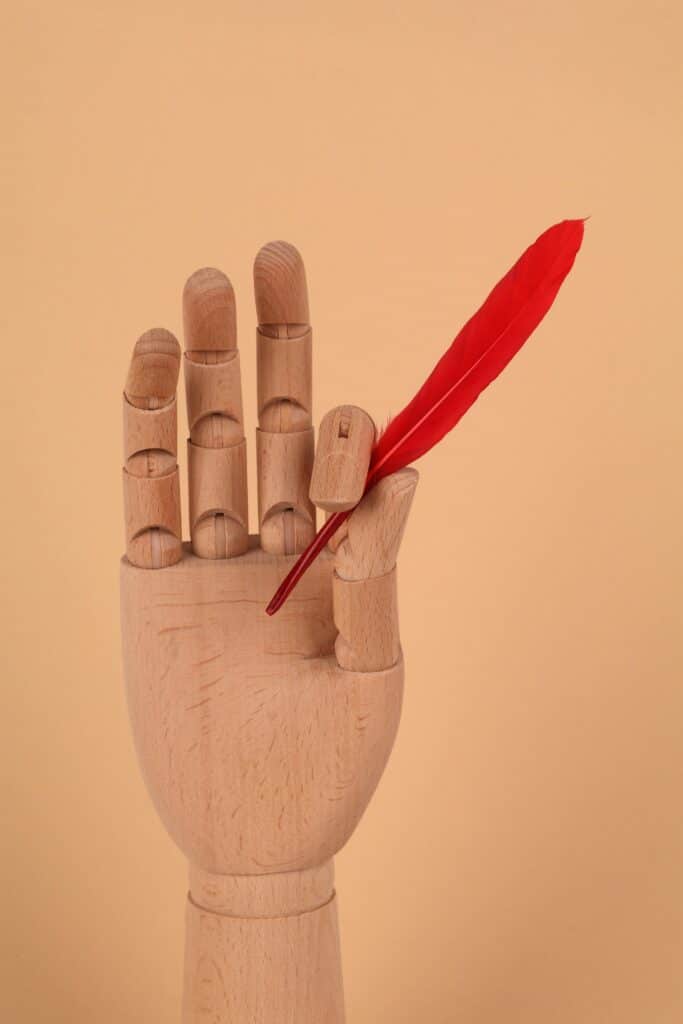 Une Autre Voix - Main en bois avec plume rouge - Une Autre Voix Une main en bois avec une plume rouge