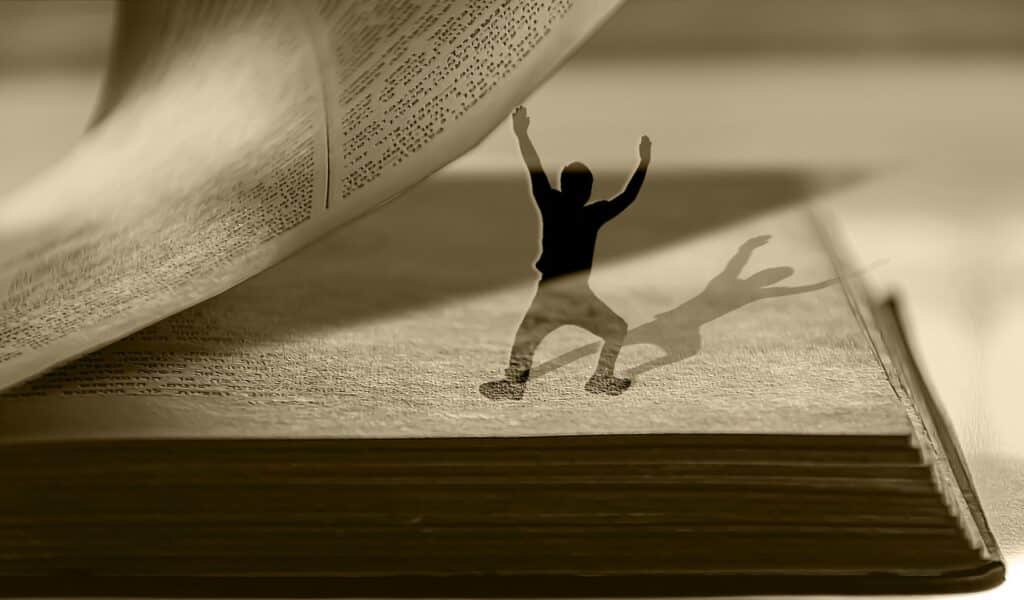 Page d'un livre soutenue par un petit homme - Une Autre Voix Page tenue par un petit homme qui lève les bras au ciel