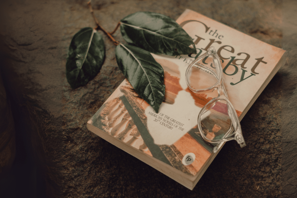 UneAutreVoix-Gatsby-Analyse-Livre - Une Autre Voix Le livre "The Great Gatsby" sur le sol avec des lunettes et des feuilles posées dessus